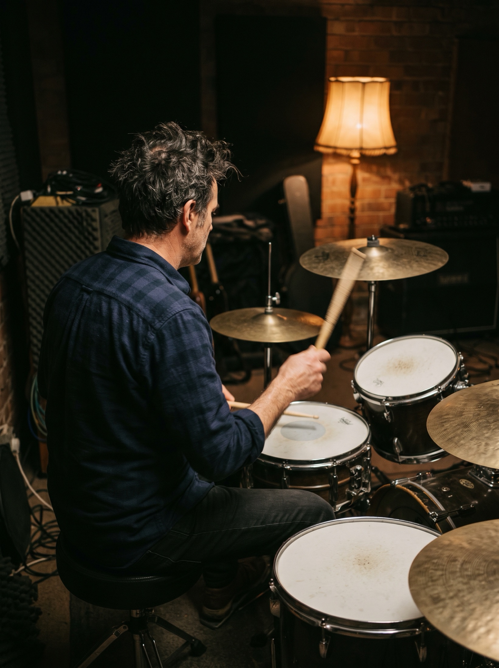 Behind a drum kit in a dim rehearsal room